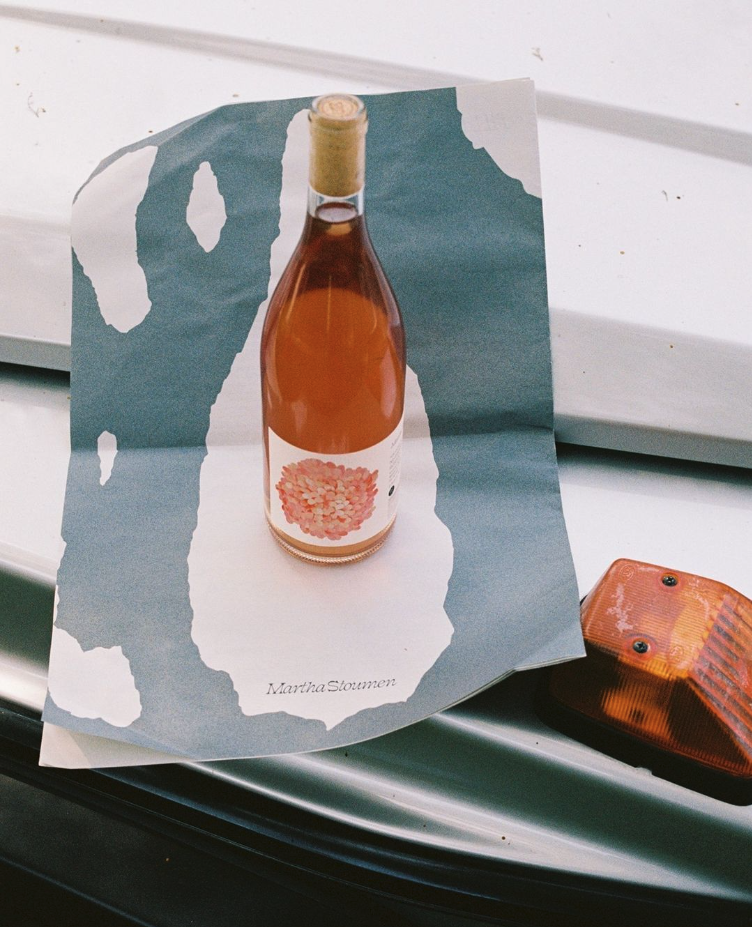 A bottle of wine sits on top of the back of the Fall / Winter 22 newsletter, mirroring the cutout